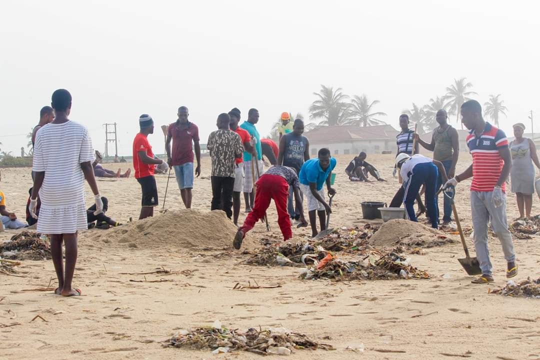 Community volunteers with shovels and brooms gather debris into piles on the beach