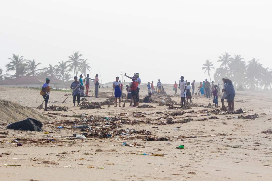 Volunteers spread across a misty Ada beach, sweeping under the palm trees
