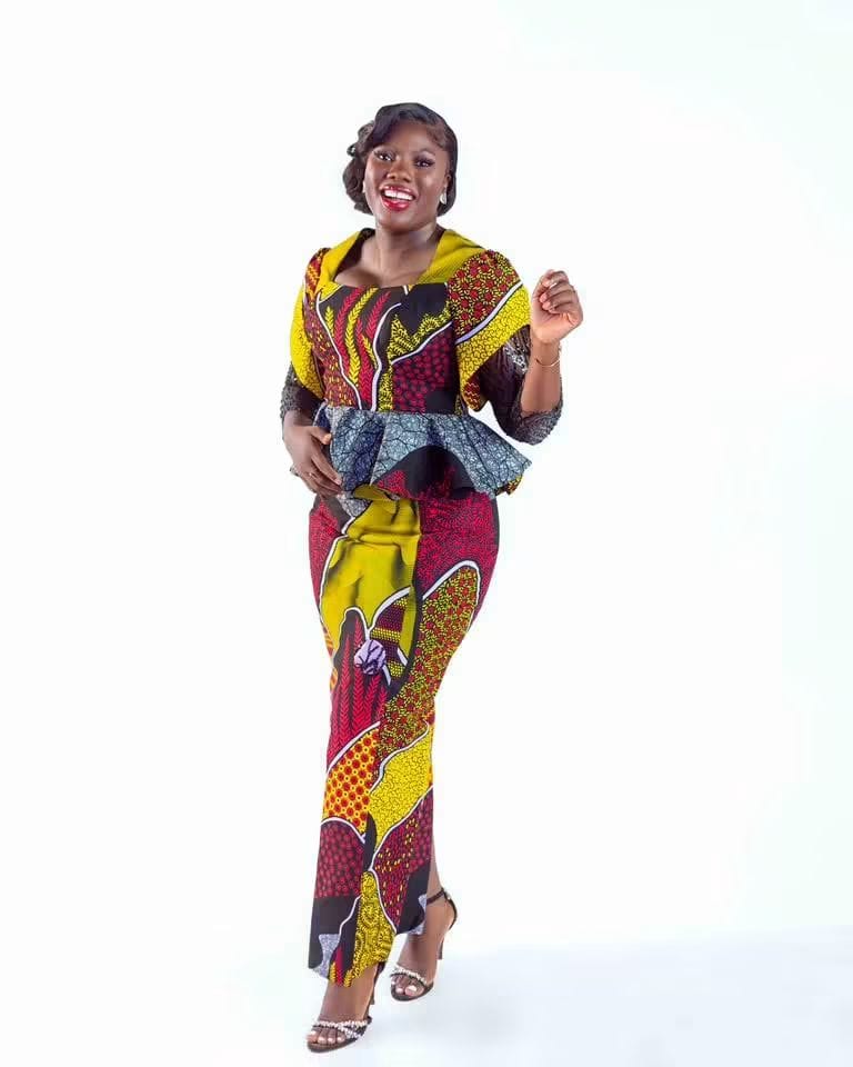 A smiling woman in a bold wax-print peplum top and skirt
