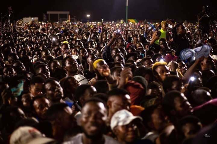 A packed night-time crowd with hands and phone lights raised toward the stage
